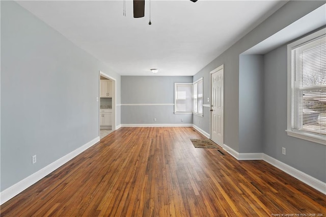 spare room with a ceiling fan, dark wood-style flooring, visible vents, and baseboards