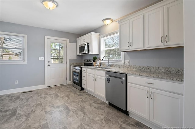 kitchen with light stone counters, stainless steel appliances, a sink, baseboards, and white cabinets