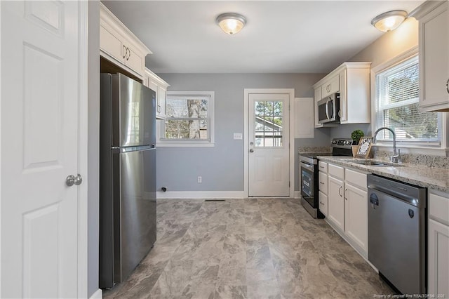 kitchen featuring light stone counters, stainless steel appliances, a sink, a healthy amount of sunlight, and white cabinets