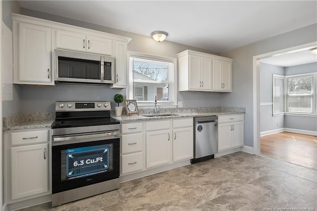 kitchen with baseboards, white cabinets, light stone countertops, stainless steel appliances, and a sink