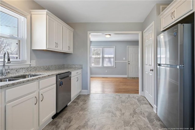 kitchen featuring appliances with stainless steel finishes, a sink, white cabinetry, and light stone countertops