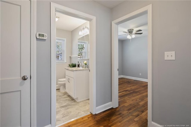 hallway with dark wood finished floors, a sink, and baseboards