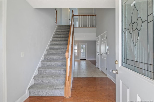 foyer entrance with stairs, a towering ceiling, light wood-style flooring, and baseboards