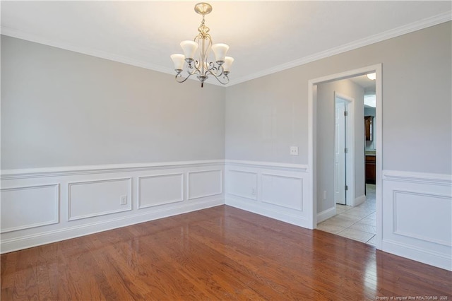 empty room featuring light wood-style floors, a chandelier, crown molding, and a decorative wall