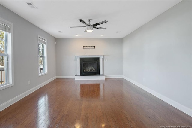 unfurnished living room with dark wood-style floors, visible vents, a glass covered fireplace, ceiling fan, and baseboards