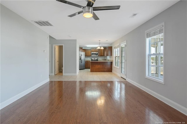 unfurnished living room with light wood-type flooring, visible vents, and baseboards