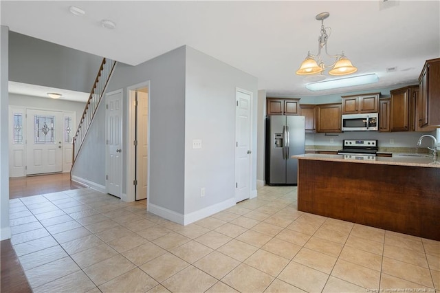 kitchen featuring brown cabinetry, appliances with stainless steel finishes, hanging light fixtures, a peninsula, and light countertops