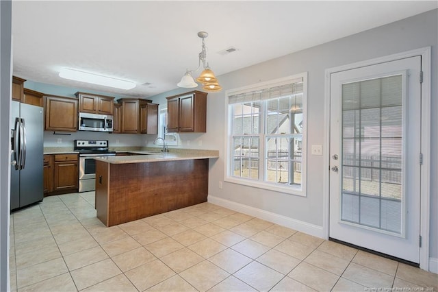 kitchen featuring brown cabinets, decorative light fixtures, light countertops, appliances with stainless steel finishes, and a peninsula