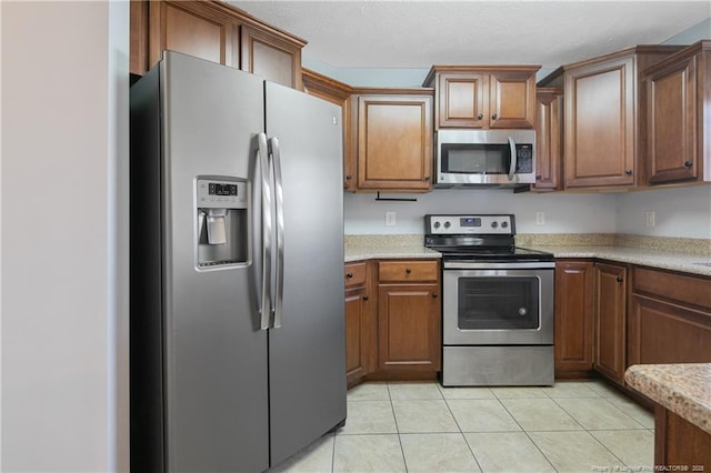 kitchen featuring stainless steel appliances, light stone countertops, brown cabinets, and light tile patterned floors