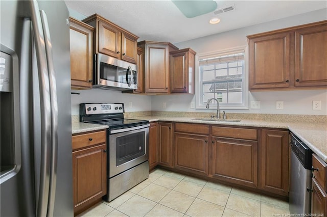 kitchen featuring stainless steel appliances, a sink, visible vents, light countertops, and brown cabinetry