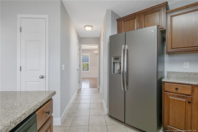 kitchen featuring light tile patterned floors, baseboards, light countertops, stainless steel refrigerator with ice dispenser, and brown cabinets