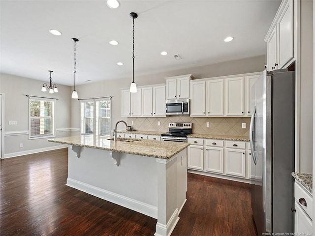 kitchen with stainless steel appliances, pendant lighting, a kitchen island with sink, and a sink