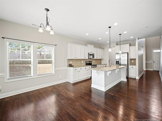 kitchen with appliances with stainless steel finishes, pendant lighting, a kitchen island with sink, and white cabinets