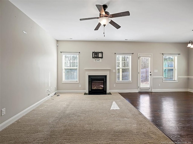 unfurnished living room with a fireplace with flush hearth, baseboards, ceiling fan, and dark wood-type flooring