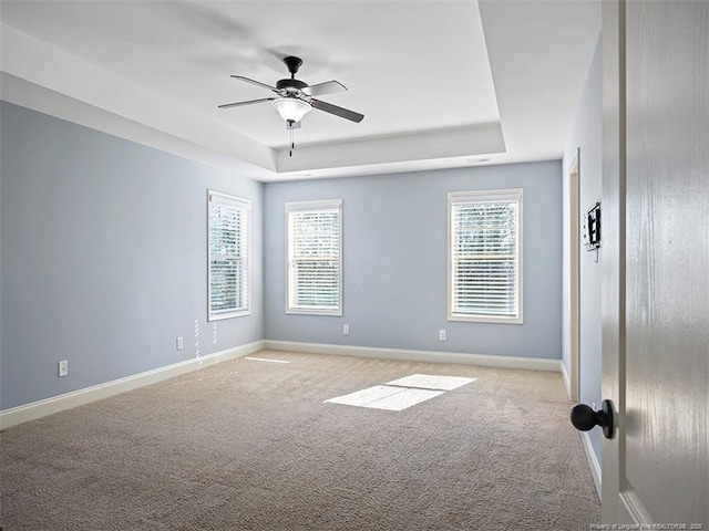 empty room with a healthy amount of sunlight, baseboards, a raised ceiling, and light colored carpet