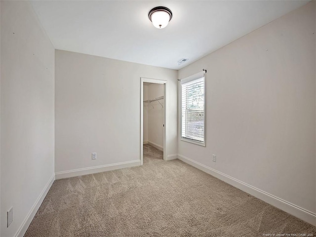 unfurnished bedroom with light carpet, visible vents, baseboards, a closet, and a walk in closet