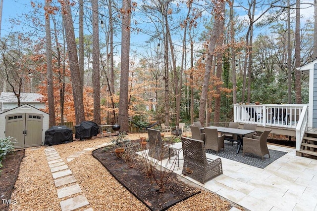 view of patio with an outbuilding, outdoor dining area, a grill, a shed, and a wooden deck