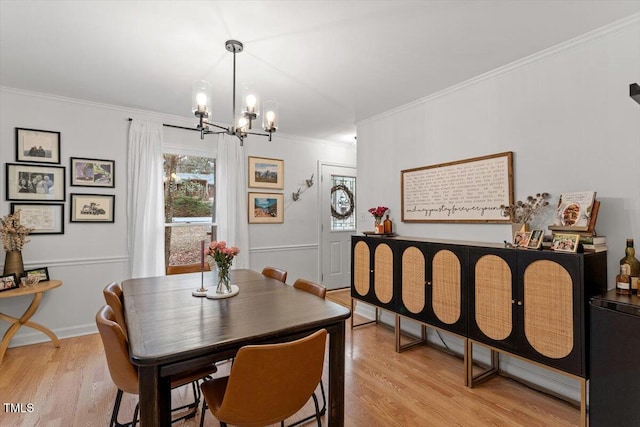 dining area featuring light wood-style floors, a chandelier, crown molding, and a wainscoted wall