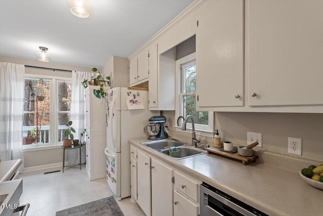 kitchen with light countertops, freestanding refrigerator, white cabinetry, a sink, and dishwasher