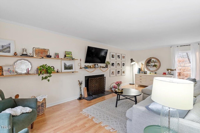 living room with a fireplace with flush hearth, crown molding, baseboards, and wood finished floors