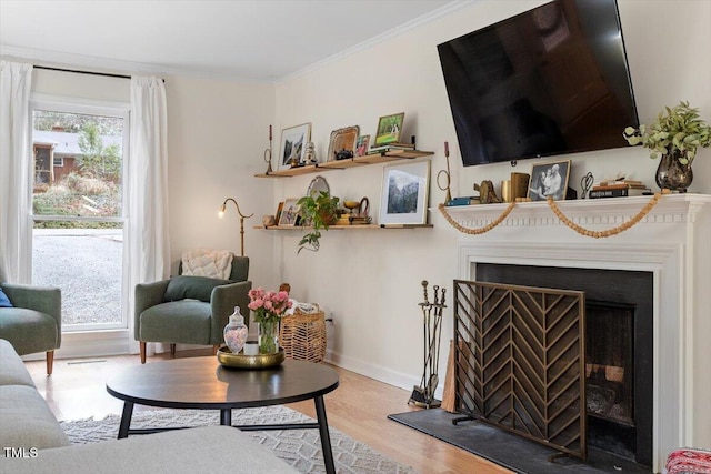 living room with light wood finished floors, baseboards, a fireplace with raised hearth, and crown molding