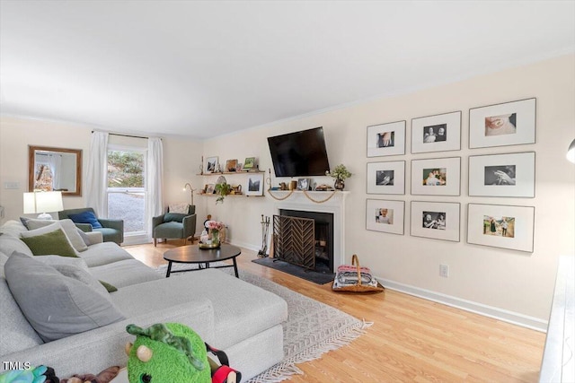 living room with a fireplace with raised hearth, crown molding, baseboards, and wood finished floors