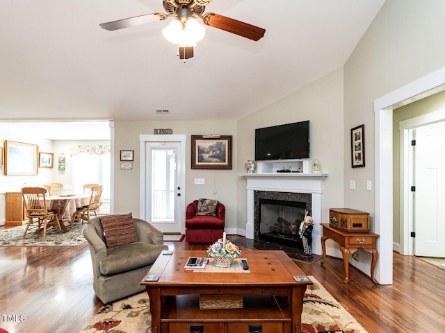 living area with baseboards, visible vents, wood finished floors, vaulted ceiling, and a high end fireplace