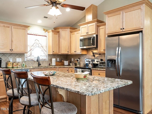 kitchen featuring lofted ceiling, light brown cabinets, stainless steel appliances, a kitchen breakfast bar, and dark wood finished floors