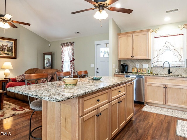 kitchen with a kitchen bar, vaulted ceiling, stainless steel dishwasher, and light brown cabinetry