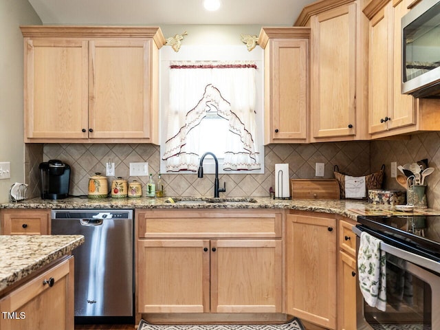 kitchen with light brown cabinets, a sink, appliances with stainless steel finishes, backsplash, and light stone countertops