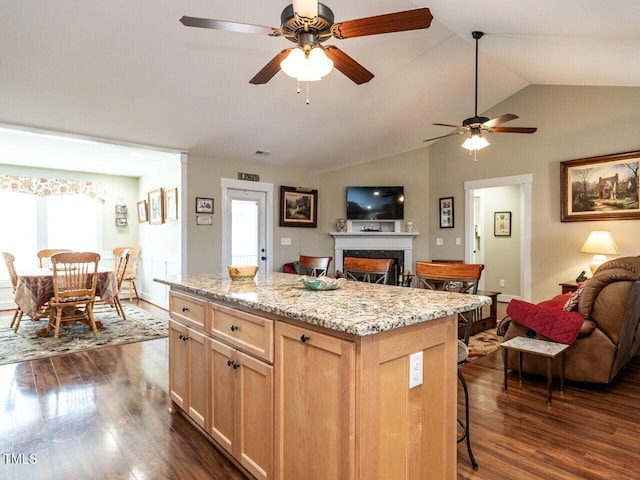 kitchen with a breakfast bar area, light brown cabinetry, dark wood-type flooring, open floor plan, and a kitchen island