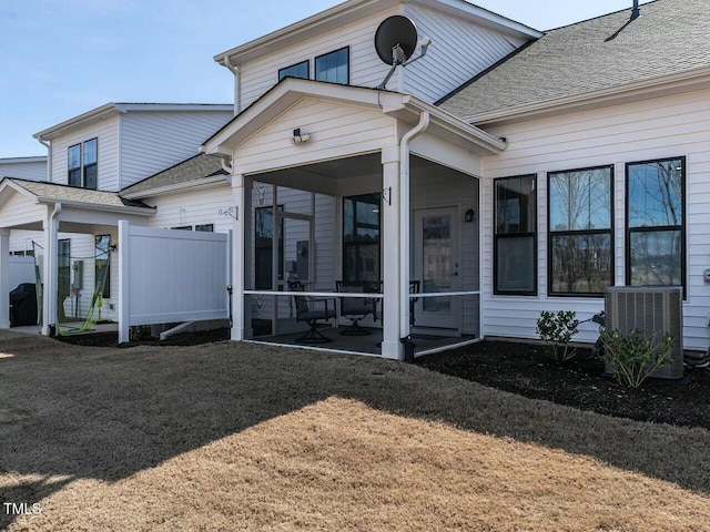 exterior space with cooling unit, a sunroom, roof with shingles, and a lawn