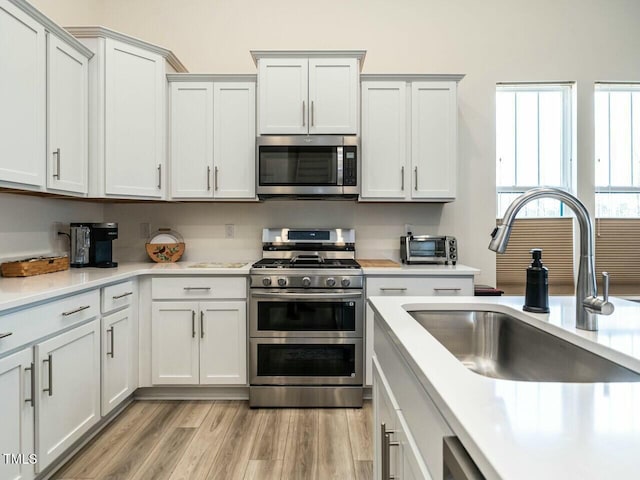 kitchen featuring light wood finished floors, a toaster, stainless steel appliances, light countertops, and a sink