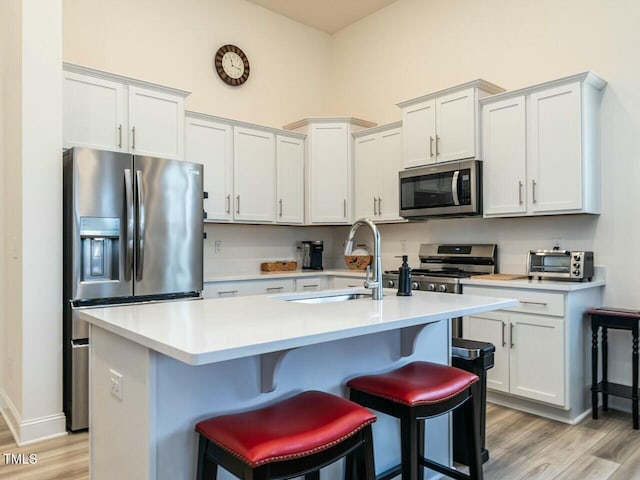 kitchen featuring an island with sink, stainless steel appliances, light countertops, light wood-style floors, and a sink