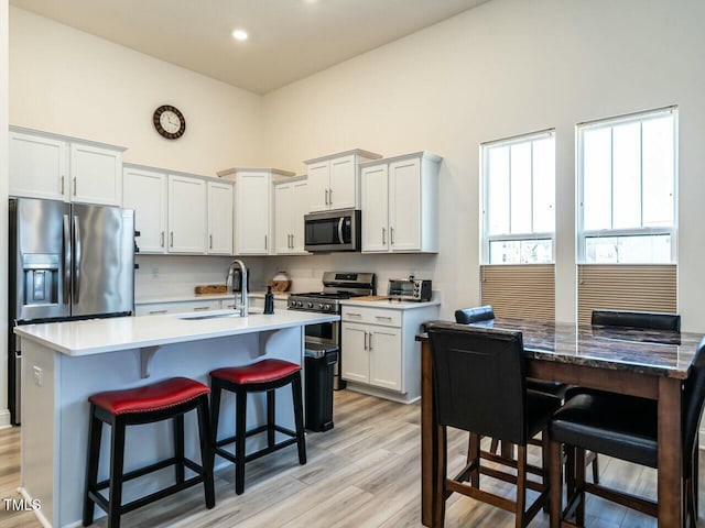 kitchen with a towering ceiling, light wood-style flooring, appliances with stainless steel finishes, a breakfast bar, and a sink