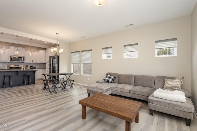 living area featuring light wood finished floors, baseboards, visible vents, and a chandelier