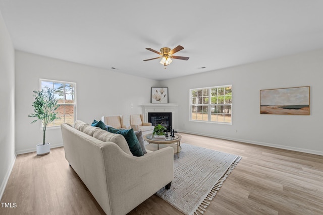 living room with a wealth of natural light, a glass covered fireplace, light wood-type flooring, and baseboards