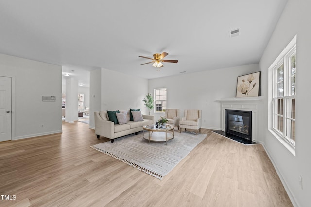 living area featuring ceiling fan, wood finished floors, visible vents, baseboards, and a glass covered fireplace