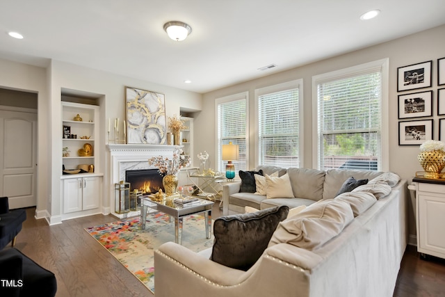 living room featuring built in features, visible vents, a premium fireplace, dark wood-style flooring, and recessed lighting