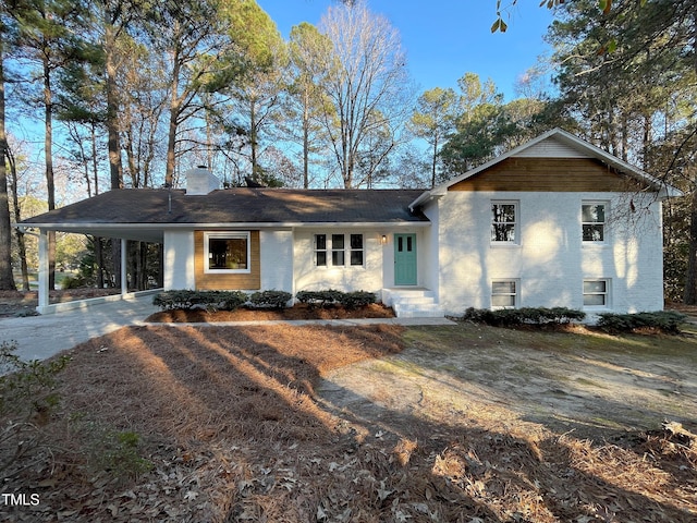 tri-level home featuring brick siding, a chimney, entry steps, an attached carport, and driveway