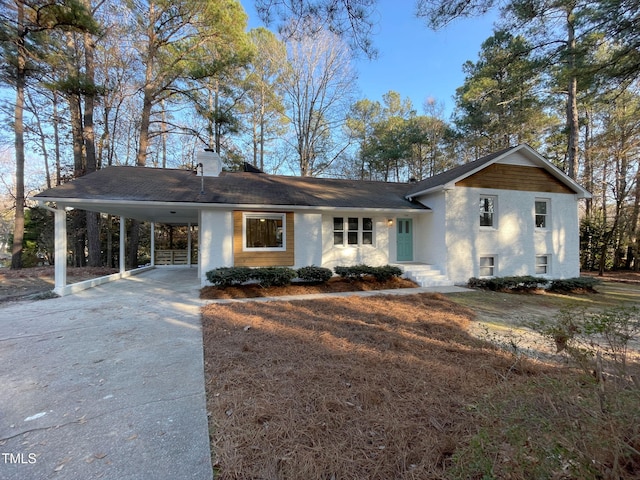 view of front of house with driveway, a carport, and a chimney