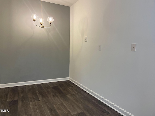 empty room with dark wood-type flooring, a notable chandelier, and baseboards