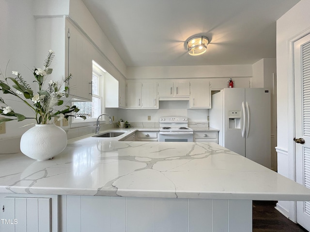 kitchen with light stone counters, white cabinetry, a sink, white appliances, and a peninsula