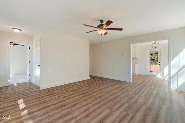 unfurnished living room featuring light wood-style floors, baseboards, and ceiling fan with notable chandelier