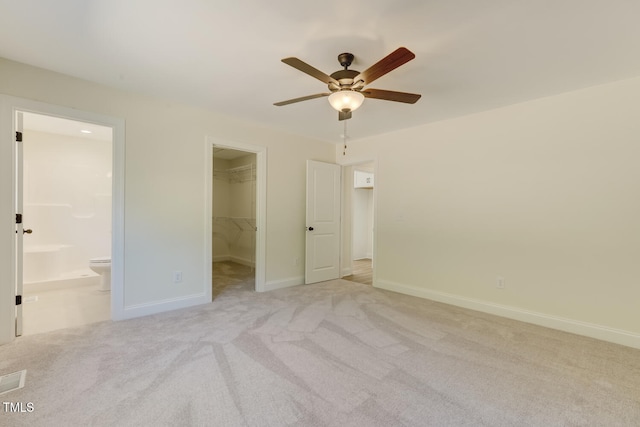 unfurnished bedroom featuring light carpet, a spacious closet, ensuite bath, and baseboards