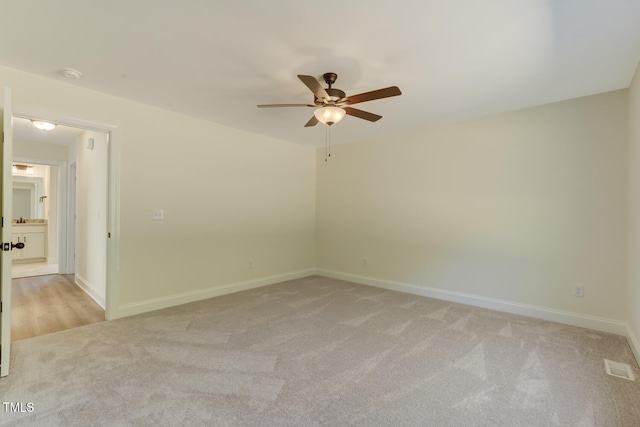 spare room with a ceiling fan, light carpet, visible vents, and baseboards