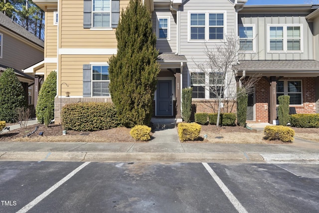 view of property with uncovered parking, board and batten siding, and brick siding