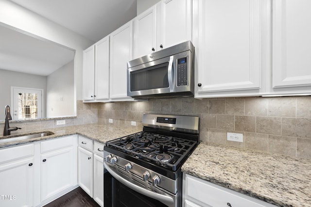 kitchen featuring white cabinets, light stone counters, a sink, stainless steel appliances, and backsplash