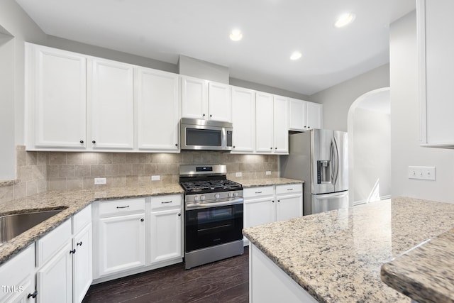 kitchen featuring arched walkways, stainless steel appliances, white cabinetry, decorative backsplash, and dark wood-style floors