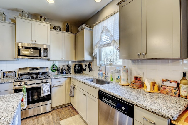 kitchen featuring light stone counters, light wood finished floors, a sink, appliances with stainless steel finishes, and backsplash